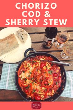 a pan filled with food sitting on top of a wooden table next to wine glasses