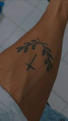 a close up of a person's arm with a cross and leaves tattoo on it