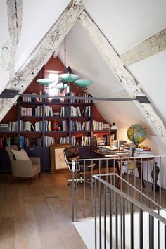 an attic office with bookshelves, desk and stairs leading up to the loft