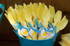 a blue bucket filled with yellow and white plastic utensils on top of a wooden table