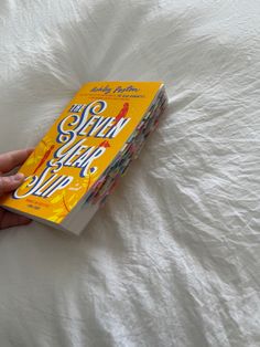 a hand holding a book on top of a white bed covered in sheets and pillows