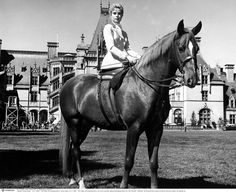 a woman riding on the back of a brown horse in front of a large building