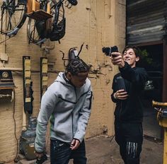 two young men standing next to each other in front of a building with bicycles hanging from the ceiling