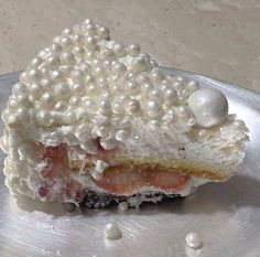 a piece of cake with white pearls on it sitting on a silver plate next to some water droplets