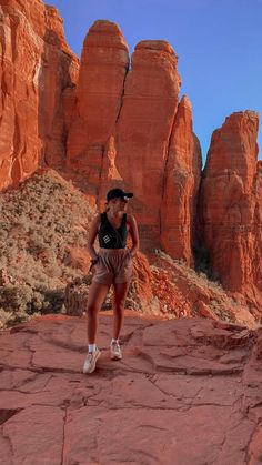 a woman standing on top of a red rock covered hillside next to tall rocky formations