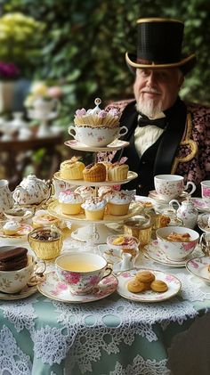 a man sitting at a table covered in tea cups and plates filled with pastries