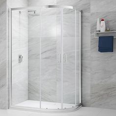 a corner shower stall in a bathroom with white marble walls and floor tiles on the wall