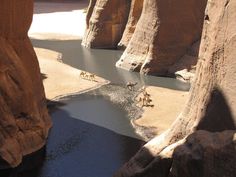 some people are riding horses in the water near large rocks and canyons that look like they're going to jump