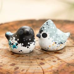 two small ceramic birds sitting on top of a tree stump, one is black and the other is white