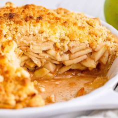 a close up of a pie in a white dish with an apple behind the pie