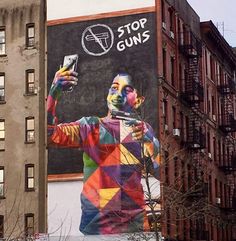 a man holding a cell phone in front of a building with a mural on it