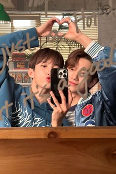 two young men taking a selfie in front of a mirror with their cell phones