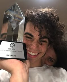 a man and woman hugging each other while holding an award in front of their face