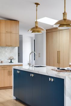 a large kitchen with blue cabinets and white marble counter tops, gold pendant lights over the island