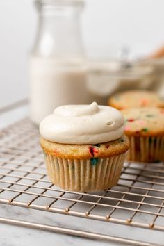 two cupcakes with white frosting on a cooling rack