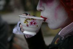 a woman with red hair and makeup drinking from a tea cup in front of her face