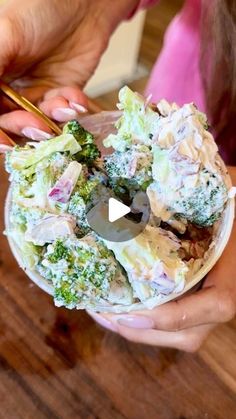 two hands holding a bowl filled with broccoli and other vegetables, while another person holds chopsticks