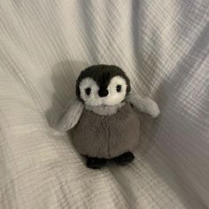 a small stuffed penguin sitting on top of a white bed sheet with eyes wide open