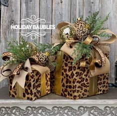 two leopard print gift boxes with bows and greenery on top, sitting on a shelf