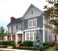 a gray house with white trim on the front door and windows is surrounded by green shrubs