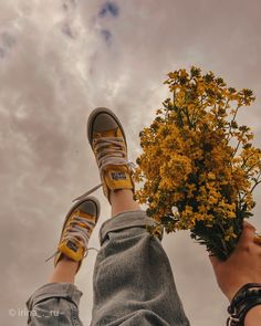 two people standing next to each other with their feet on the ground holding yellow flowers