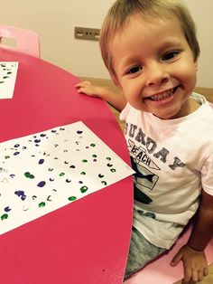 a little boy sitting at a pink table smiling