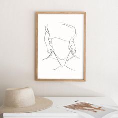 a hat is sitting on a table next to a framed drawing