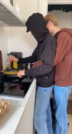 two young men standing in front of an oven cooking food on the stove burners