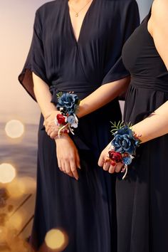 two women in black dresses holding bouquets of blue and red flowers on their hands