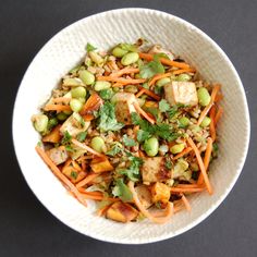 a white bowl filled with carrots, peas and tofu mixed in sauce on top of a black table