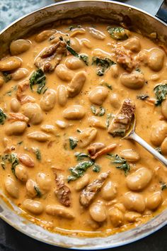 a pot filled with beans and spinach on top of a table next to a spoon