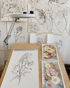 several drawings are being displayed on a table with a lamp in the background and flowers drawn on paper