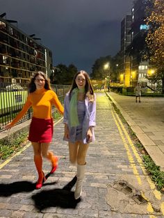 two young women walking down a sidewalk at night with their hands in each others'pockets