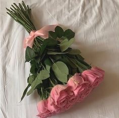 a bouquet of pink roses and green leaves on a white sheet with the stems still attached