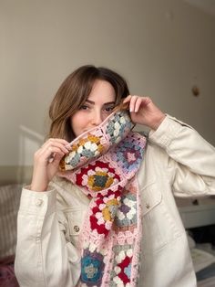 a woman holding up a crocheted scarf in front of her face