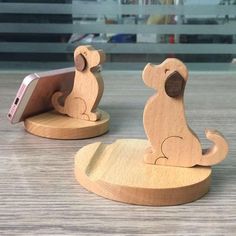 two wooden toy animals sitting next to each other on top of a wood table with a cell phone in the holder