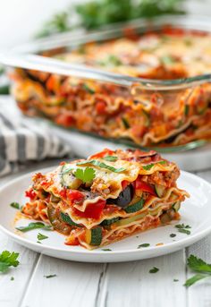 a white plate topped with layered lasagna next to a casserole dish