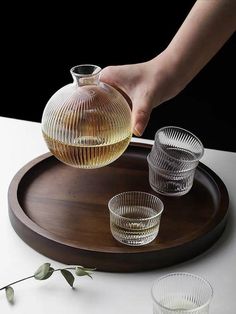 a person is pouring water into two glasses on a tray with a wooden serving tray