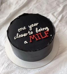 a black cake with white frosting and red writing on the top that says, one year closer to being a mile