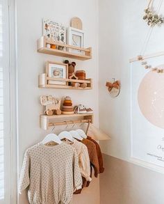 a white room with shelves and pictures on the wall, clothes hanging in front of them