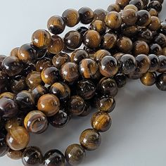 Tiger's Eye C Quality natural stone beads, 8mm. MOHS hardness:  7 Stone of Courage. Roman soldiers wore engraved Tiger's eye to protect them in battle. Some say it enhances personal empowerment and inner strength.  Said to act as a shield, deflecting negative energies and promoting mental clarity and focus. My goal is to consistently provide the best beads available.  You'll always receive excellent quality beads from me and I will never lie to you about their grade.  Our photos are taken in-house so you'll always see what you're getting.   Details: - Strand length: approximately 15" - Price is per strand. - Bead sizes are approximate and may have a variation of +/- 0.5mm. - Drill hole sizes on MOST beads - 4mm beads: about 0.5mm; 6-8mm beads: about 0.7-0.8mm; 10-12mm beads: about 0.8-1.0m Personal Empowerment, Brown Gemstone, Tiger Eye Beads, Natural Beads, Tiger Eye, Crystals And Gemstones, Stone Beads, Round Beads, Natural Stones