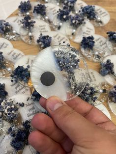 a person is holding an object in front of some blue and white flowers on a table