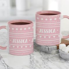 two pink coffee mugs sitting on top of a counter next to marshmallows