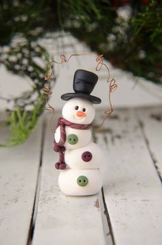 a small snowman with a top hat and scarf on it's head is standing next to a plant