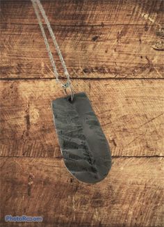 a piece of metal sitting on top of a wooden table next to a necklace hanging from a chain