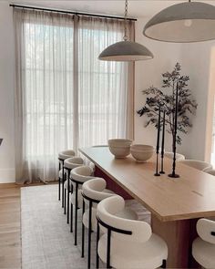 a dining room table with chairs and vases on top of it, in front of a large window