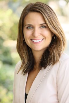 a woman with long hair smiling at the camera and wearing a white blazer jacket