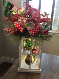 a christmas centerpiece with ornaments and lights in it on a wooden table next to a window