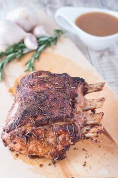 a piece of meat on a wooden cutting board next to garlic and gravy