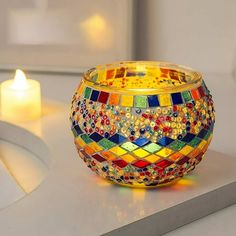 a colorful glass candle holder sitting on top of a counter next to a lit candle